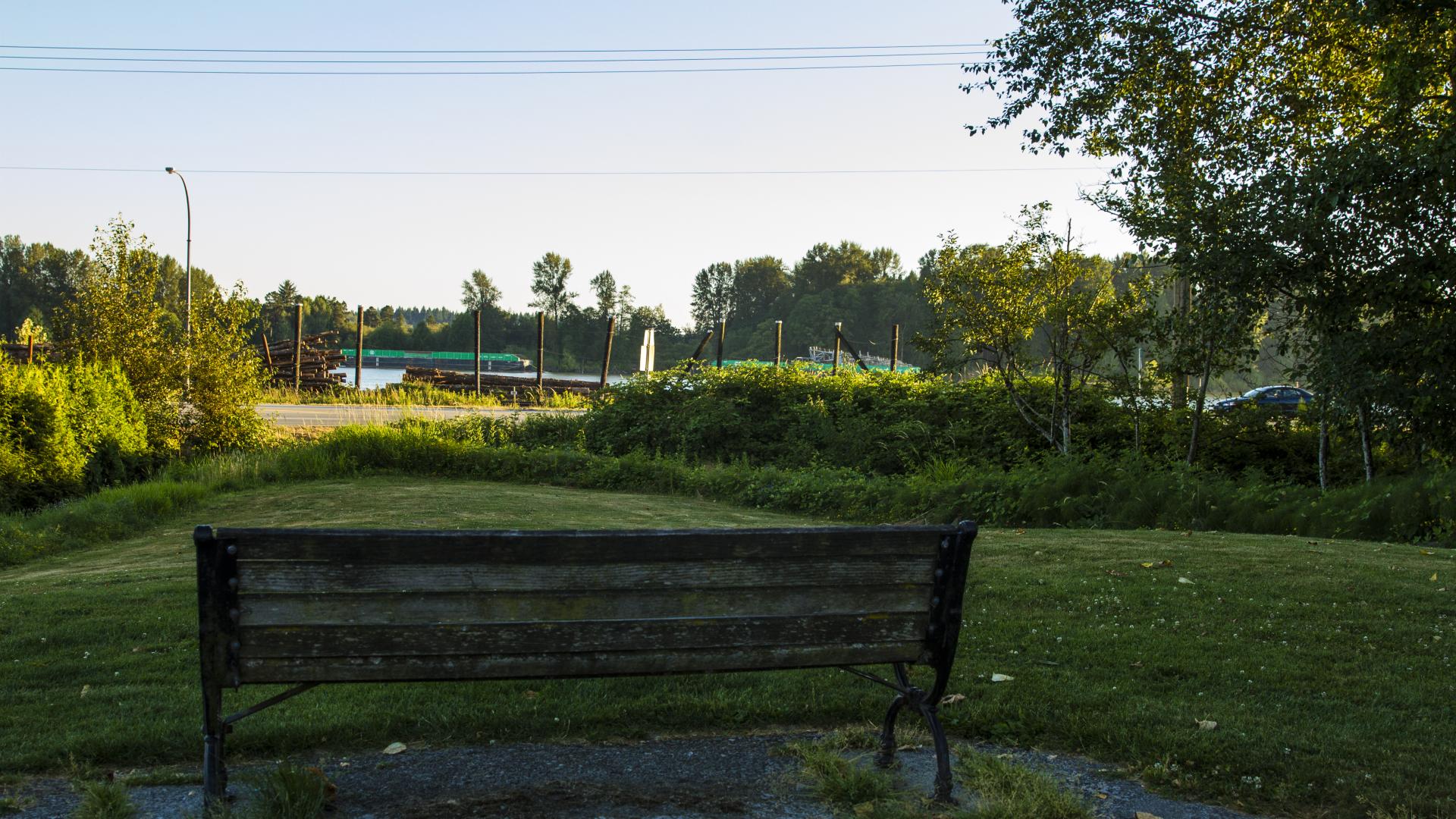 A bench sits on the edge of a paved path, overlooking a grassy field. 